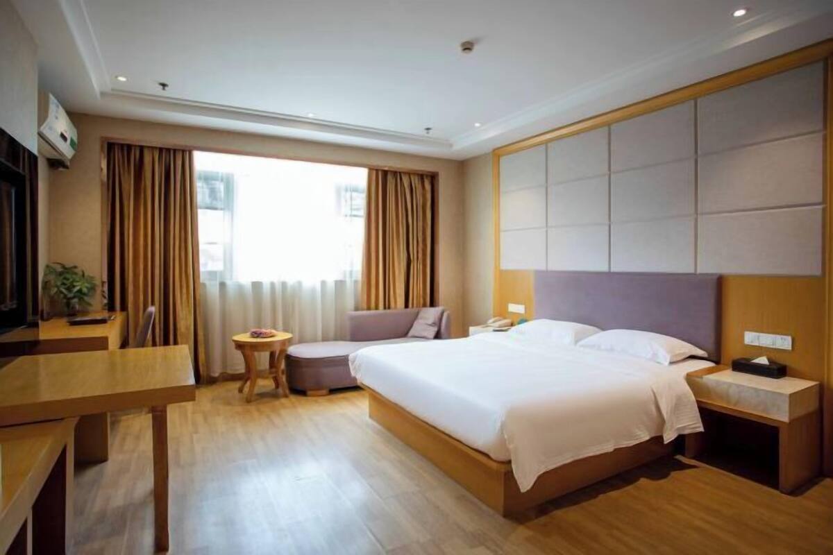 Et hotelværelse med seng, sengebord, lampe og et vindue med gardiner.