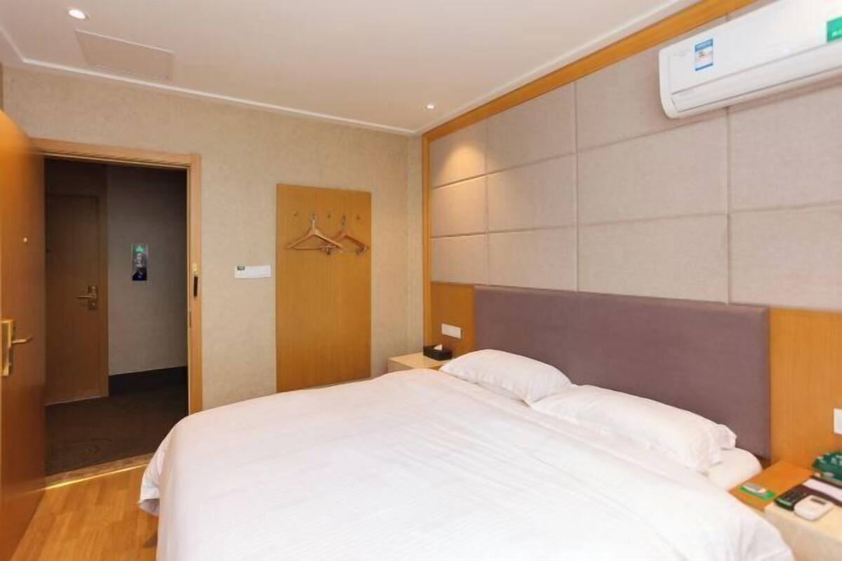 Et hotelværelse med en seng, et natbord, et knagered og en aircondition.