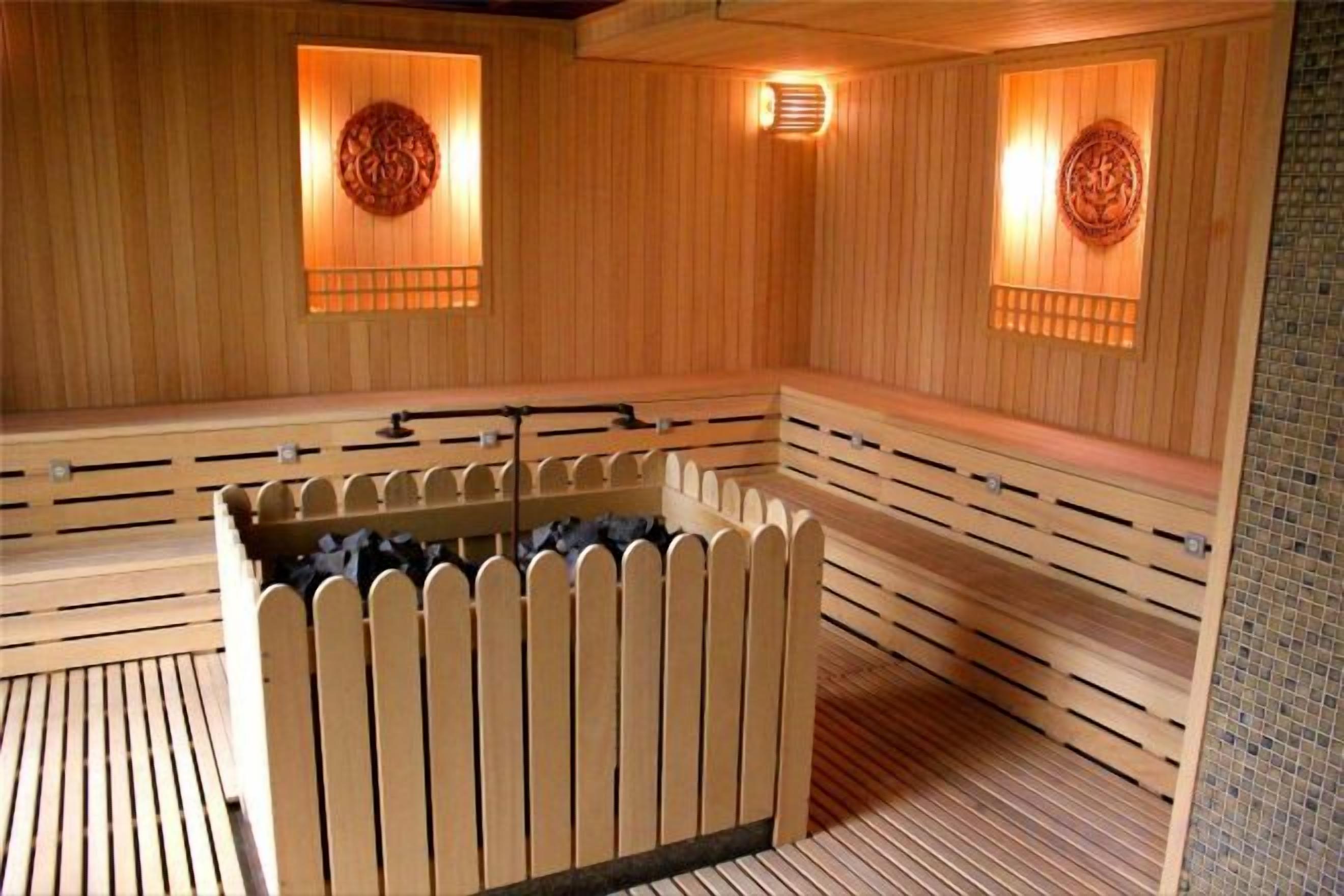A sauna with wooden benches and a central heated floor, featuring wall-mounted light fixtures.