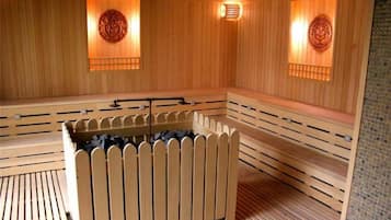 A sauna with wooden benches and a central heated floor, featuring wall-mounted light fixtures.