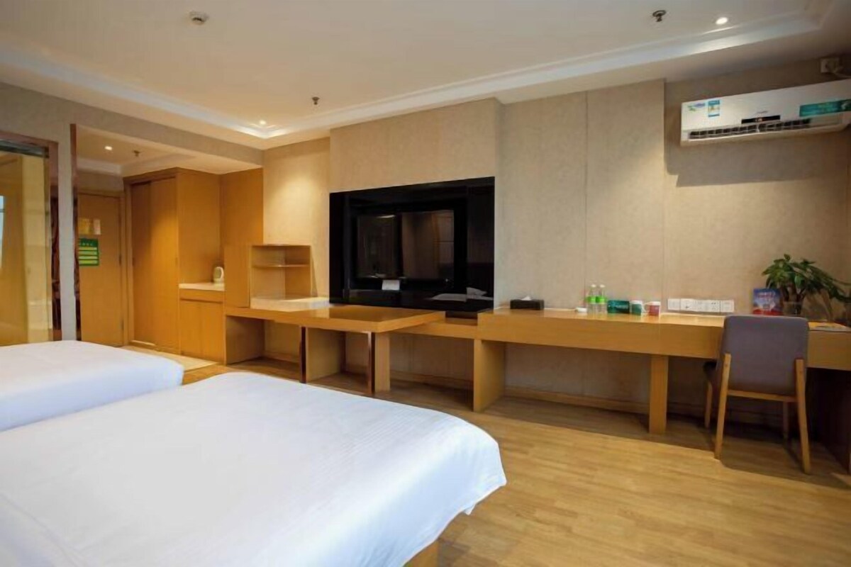 A hotel room with two beds, a desk, a television, and an air conditioning unit.