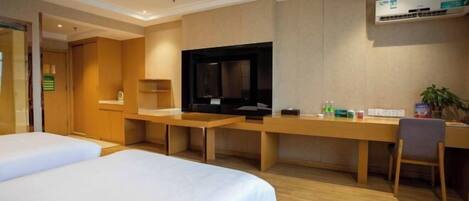 A hotel room with two beds, a desk, a television, and an air conditioning unit.