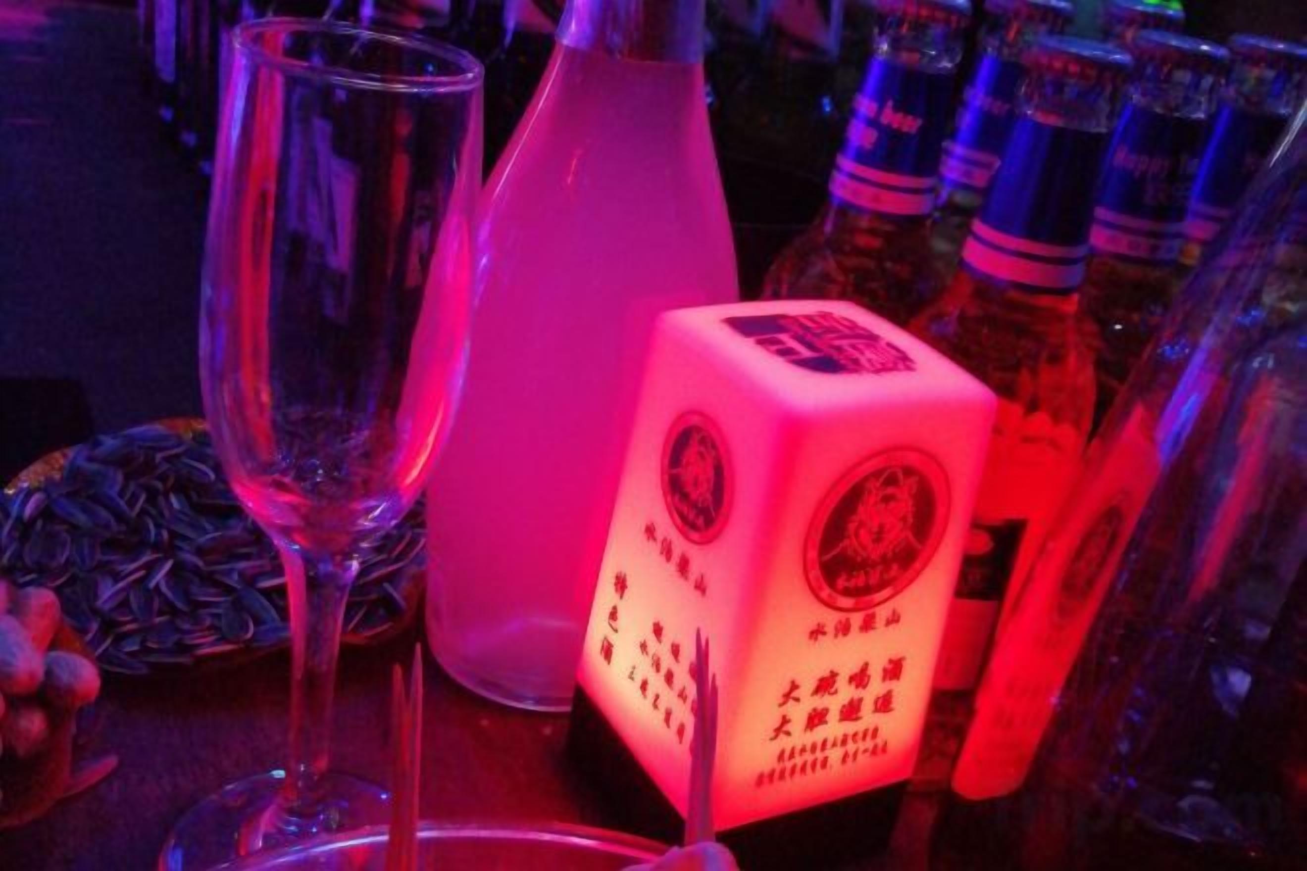 A dice, a bottle, and a glass on a table with bottles in the background.