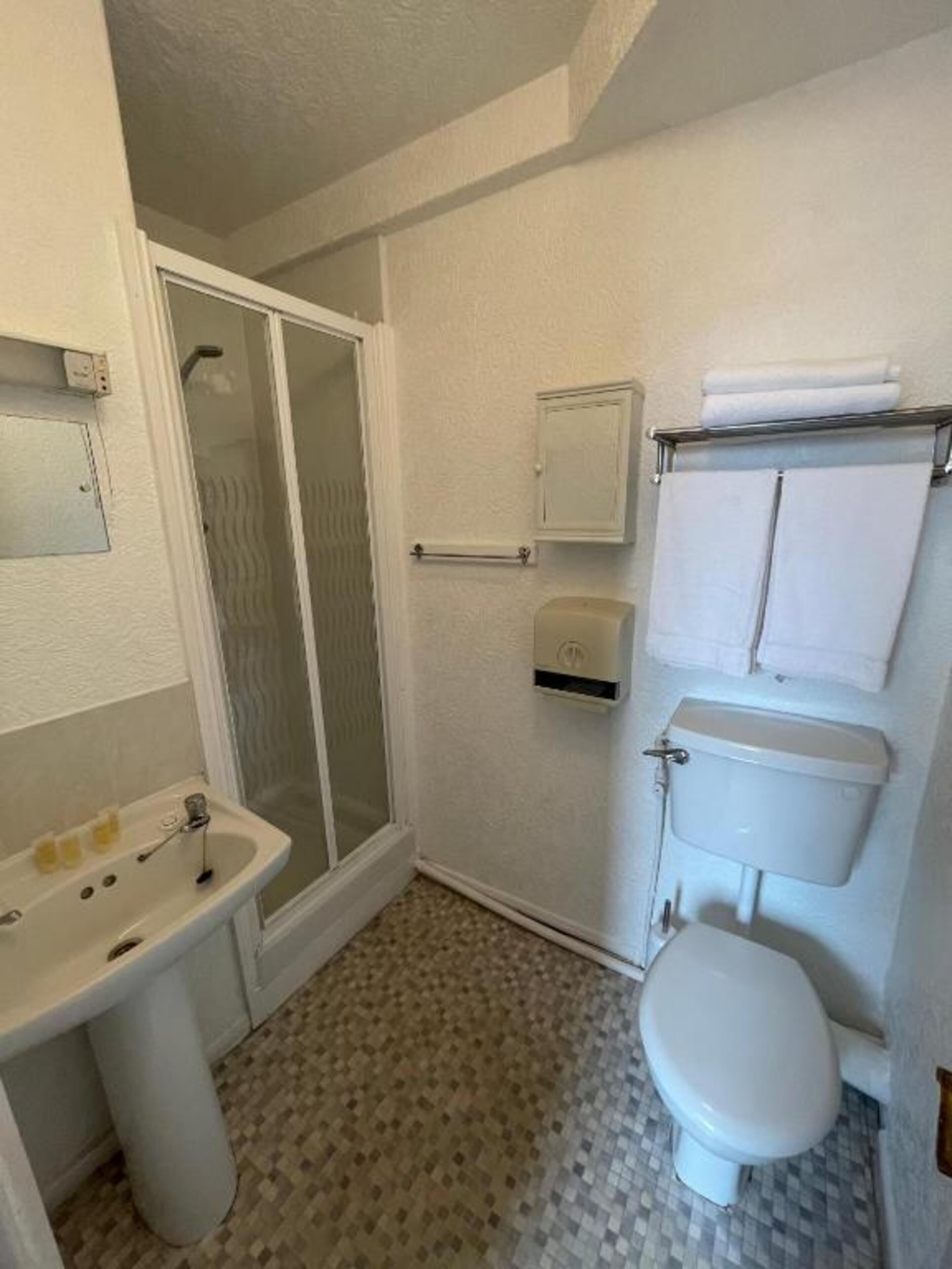 Egy fürdőszoba zuhanyzóval, WC-vel, mosdókagylóval és törölközőtartóval.