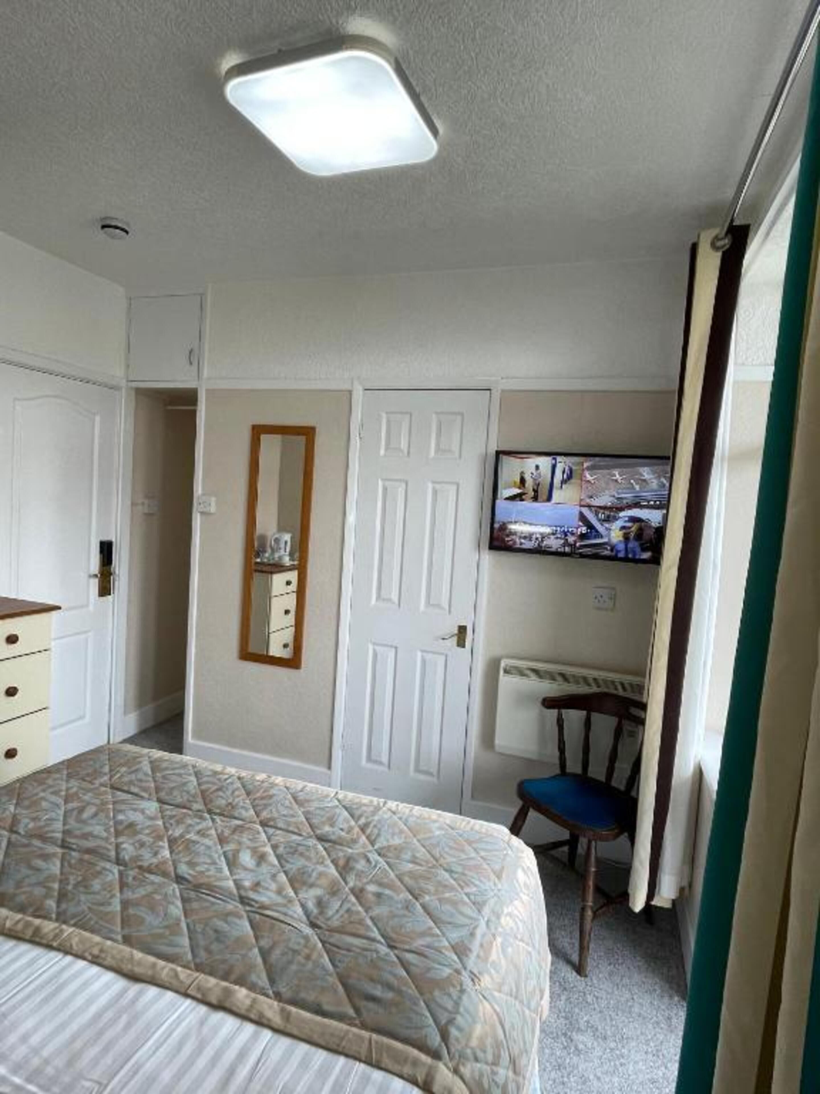 A bedroom with a bed, a dresser, a mirror, a door, a radiator, and a television on the wall.
