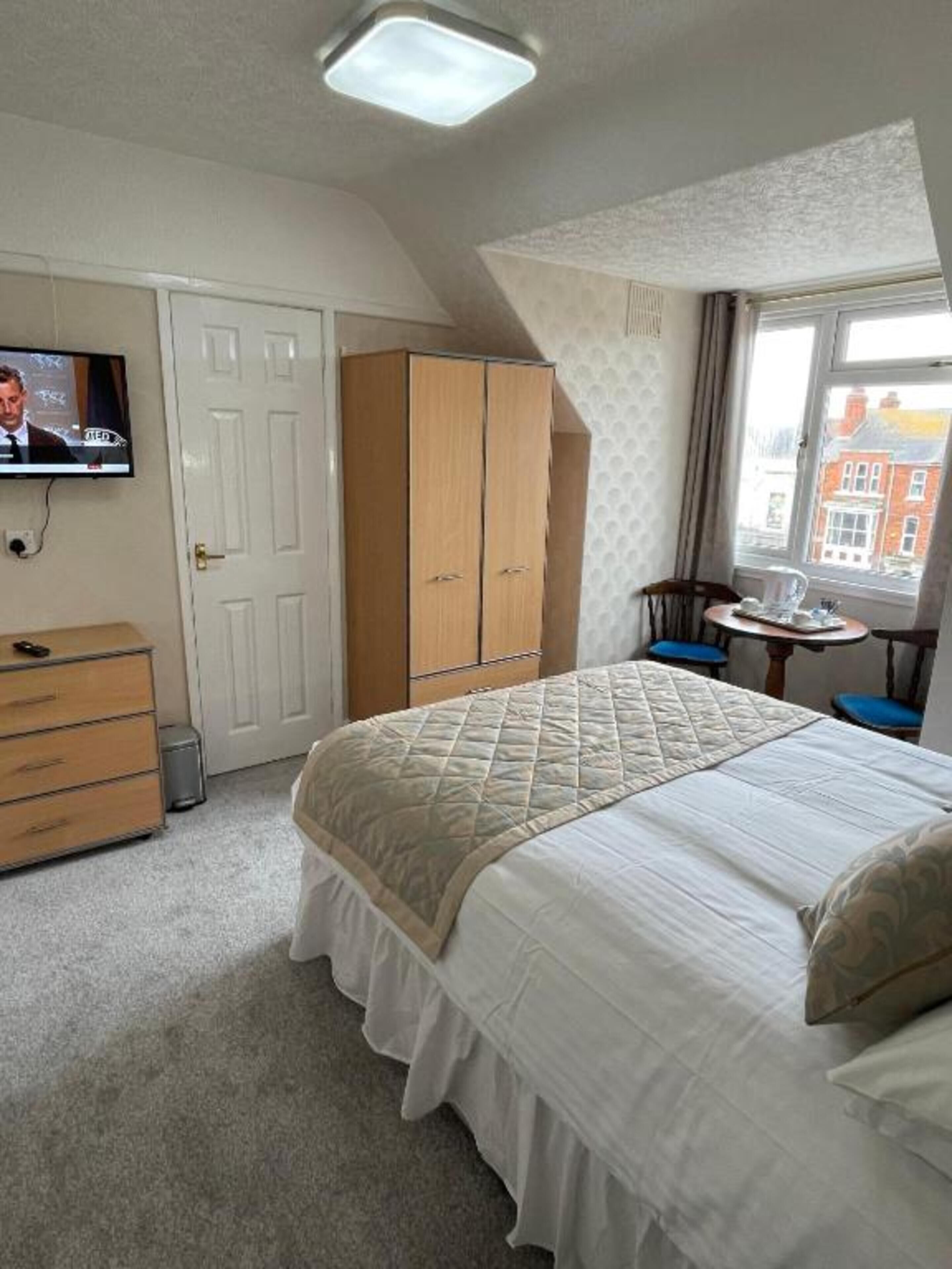 A bedroom with a bed, a wardrobe, a television, and a window with a view of buildings.