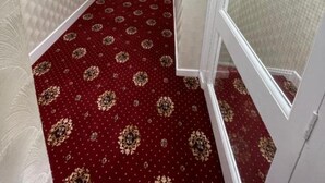 Um corredor com carpete estampado, paredes brancas e uma porta no final.