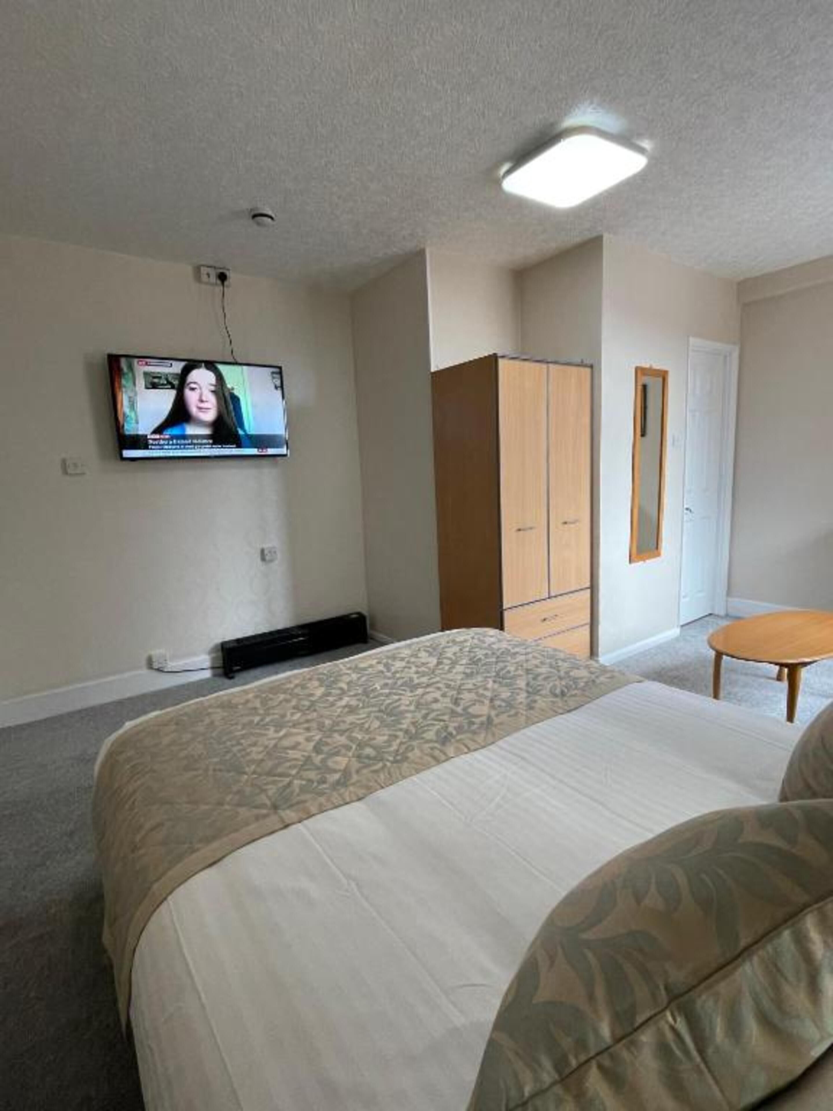 A hotel room with a bed, a television mounted on the wall, a wardrobe, and a small round table.