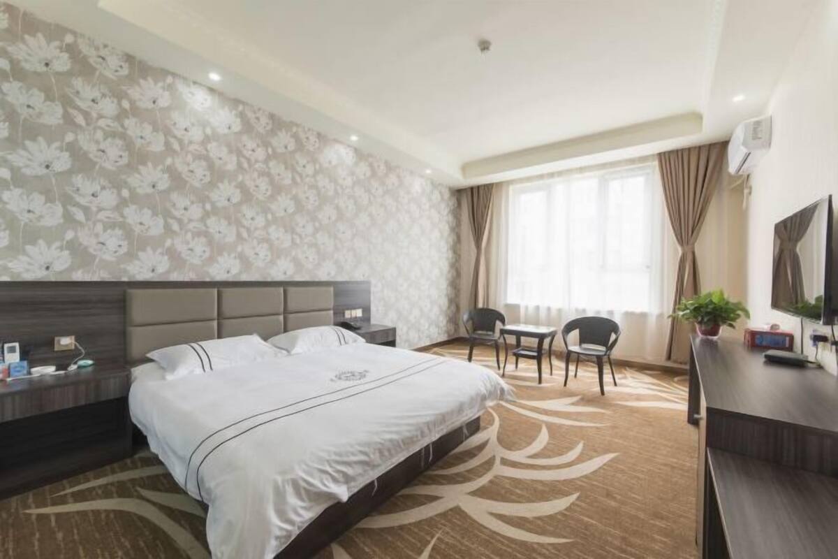 A hotel room with a large bed, a desk, a chair, a TV, and a window with curtains.