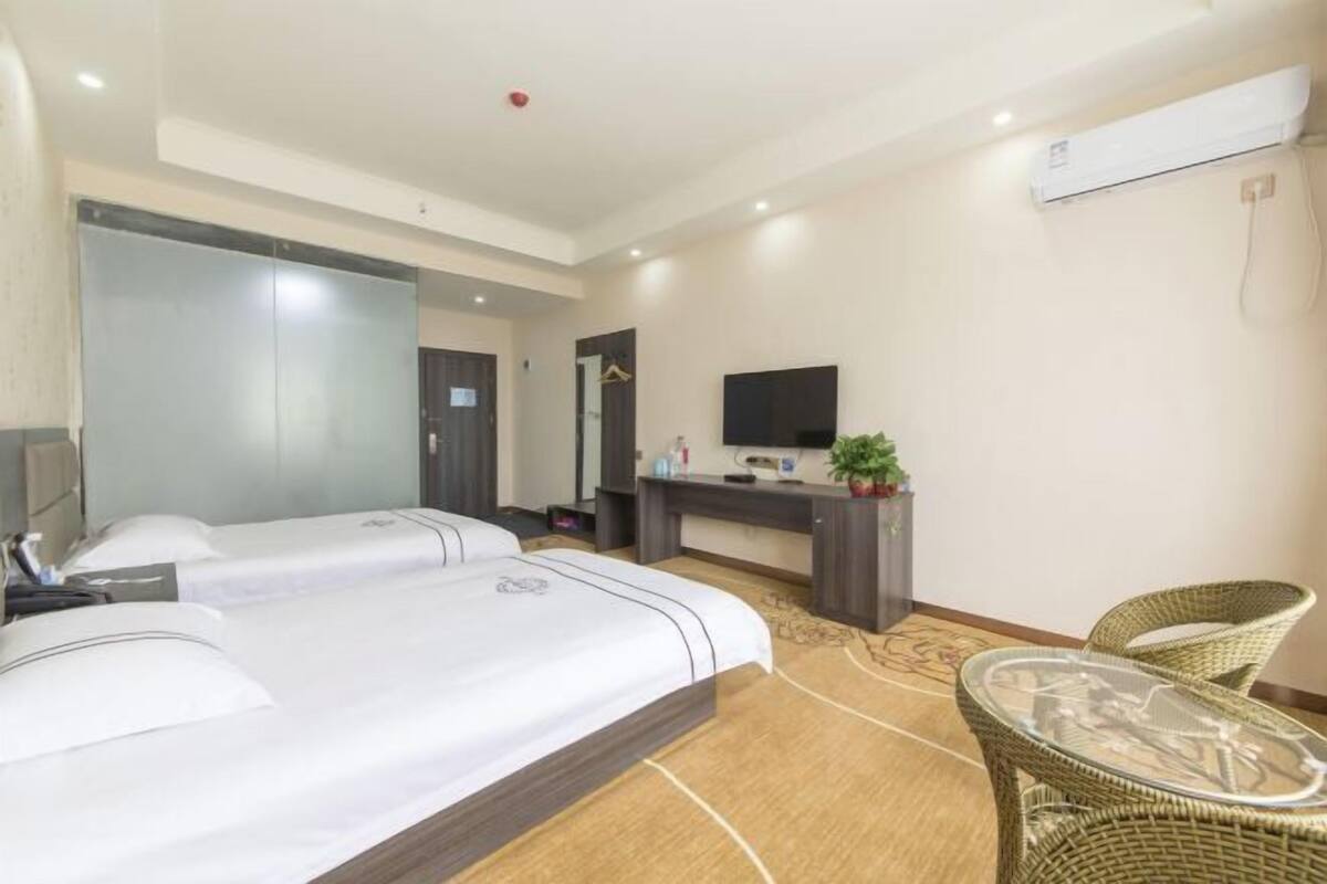 A hotel room with two beds, a desk, a TV, a chair, and a small table.