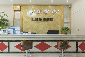 A hotel reception desk with a clock, a computer, and a plant. - Huijia Express Hotel (Luoyang)