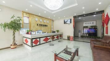 A hotel reception area with a reception desk, a chandelier, a television, and a seating area.