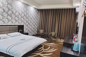 A hotel room with a bed, a small table with chairs, a wall with a floral pattern, and a curtain. - Huijia Express Hotel (Luoyang)