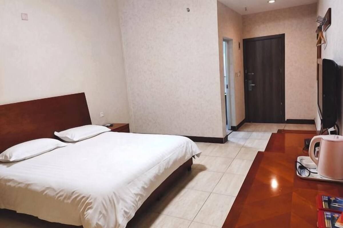 A hotel room with a bed, a coffee table, a TV, and a door leading to a hallway.