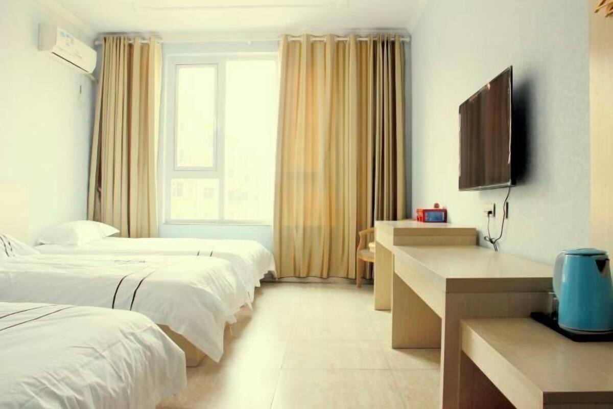 A hotel room with two beds, a desk, a television, and a window with curtains.