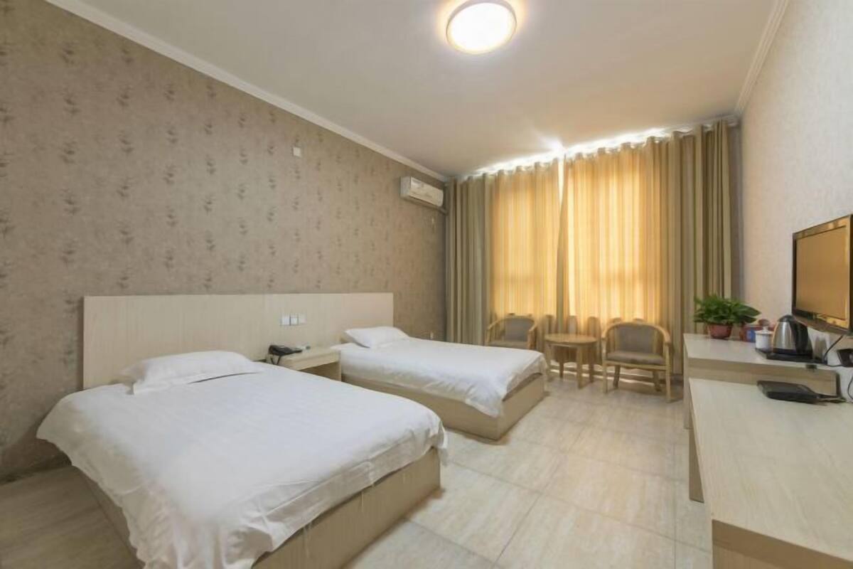 A hotel room with two beds, a desk, a chair, a TV, and a window with curtains.