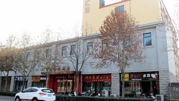A building with multiple storefronts, a parked car, and a tree in front.