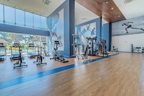 Un gimnasio amplio con máquinas de cardio, pesas y un gran mural de un corredor.