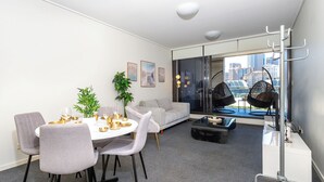 Una sala de estar moderna con comedor, un sofá, una mesa de centro y vistas a la ciudad a través de amplios ventanales.