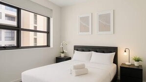Una cama bien hecha con ropa blanca, un cabecero negro y dos cuadros en la pared.