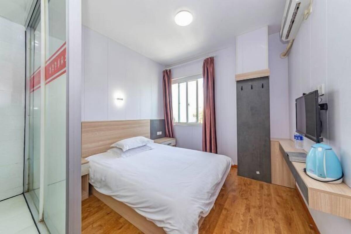 A hotel room with a bed, a desk with a computer, a TV, and a window with curtains.