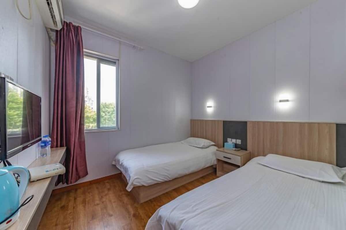 A hotel room with two beds, a TV, a desk with a kettle, and a window with curtains.