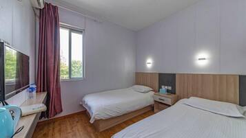 Habitación de hotel con dos camas, un televisor, un escritorio con hervidor y una ventana con cortinas.
