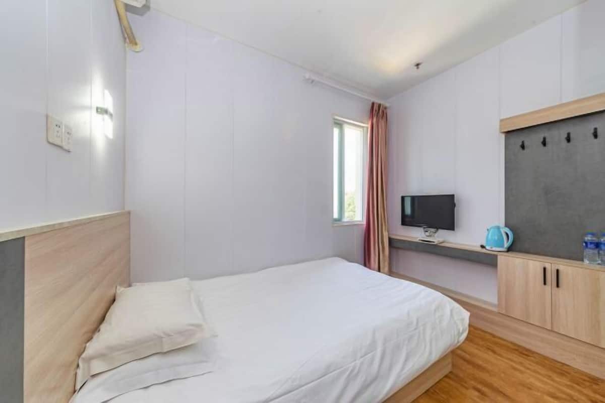 A bedroom with a bed, a television, a kettle, and a water bottle on the nightstand.