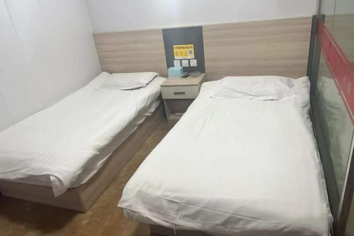 A room with two single beds, a small bedside table with a lamp, and a wall-mounted sign.
