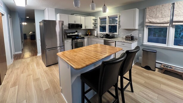 Een moderne keuken met witte kasten, een houten eiland met barstoelen, roestvrijstalen apparatuur en een groot raam met uitzicht.