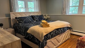 Een slaapkamer met een bed, nachtkastje, kaptafel en een raam met gordijnen.