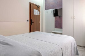 A bedroom with a bed, a wooden door, a white wardrobe, and a wall-mounted TV. - Hotel 3 Your Haven of Peace in Ventimiglia (Ventimiglia)