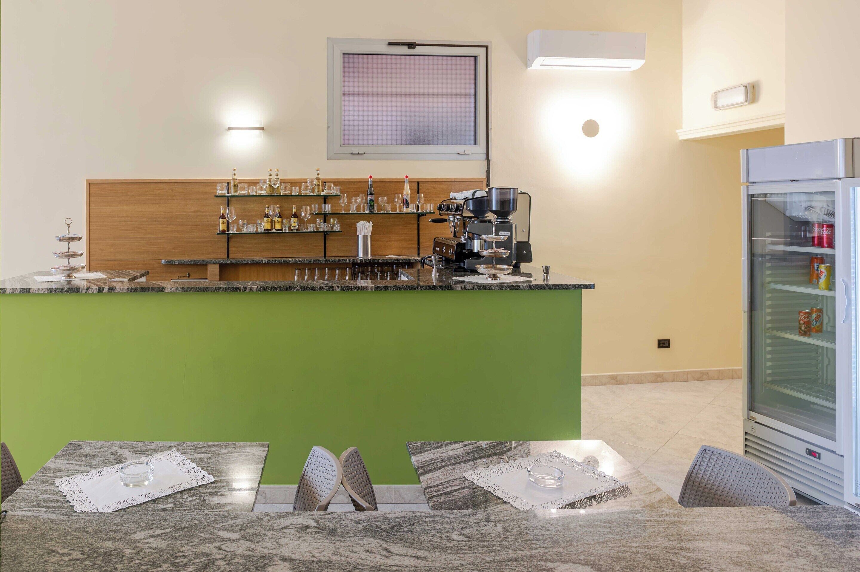 Un espace bar avec un comptoir vert, une machine à café et des étagères remplies de bouteilles et de verres.