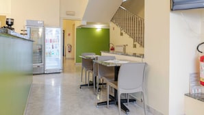 A kitchenette with a refrigerator, microwave, and coffee maker. There are two chairs and a table with a glass top. A fire extinguisher is mounted on the wall. - Hotel 3 Your Haven of Peace in Ventimiglia (Ventimiglia)