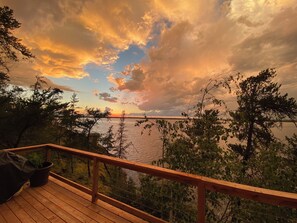 Um deck de madeira com vista para um corpo d'água e árvores ao fundo.