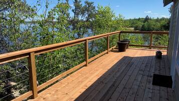 Une terrasse en bois avec une rambarde donnant sur une étendue d’eau, entourée d’arbres.