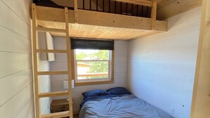 Una habitación pequeña de madera con una litera, una ventana y una escalera.