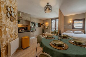 Une chambre d’hôtel compacte dotée d’une kitchenette, d’un coin repas avec une table dressée pour deux personnes et d’un lit offrant une vue agréable.