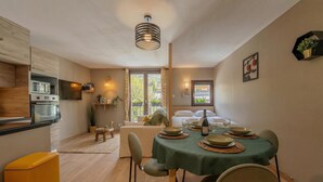 A compact kitchen with modern appliances, a dining area with a table set for two, and a cozy seating area with a sofa and a small side table.