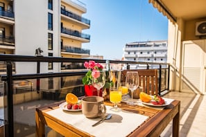 A balcony with a table set for breakfast, including a mug, orange juice, and fruit.