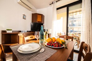 Un coin repas avec une table dressée pour deux personnes, un téléviseur et une fenêtre avec des rideaux.