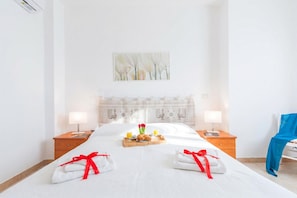 A hotel room with a large bed, two bedside tables, a headboard with a floral painting, and a blue chair.