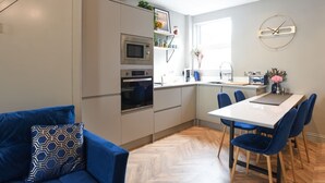 Una cocina moderna con electrodomésticos integrados, un comedor con sillas azules y un sofá con cojines estampados.