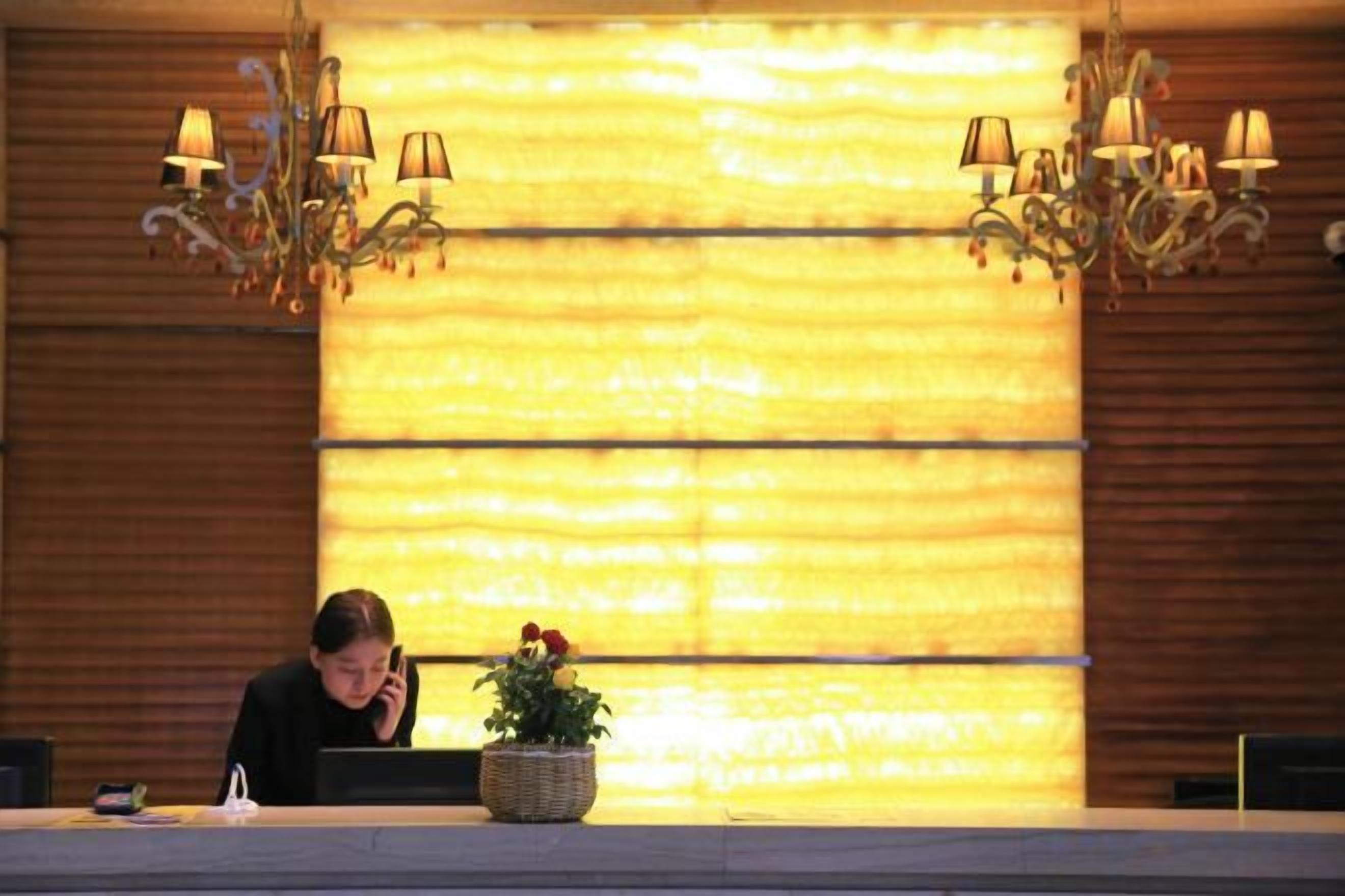A reception desk with a plant, a chandelier, and a wooden wall.