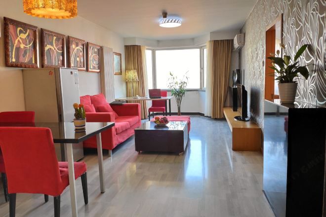 A modern living room with a dining area, red furniture, a flat-screen TV, and artwork on the walls.