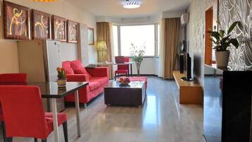 A modern living room with a dining area, red furniture, a flat-screen TV, and artwork on the walls.