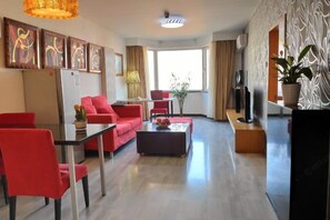 Un salon moderne comprenant un coin repas, des meubles rouges, un téléviseur à écran plat et des œuvres d’art accrochées aux murs.