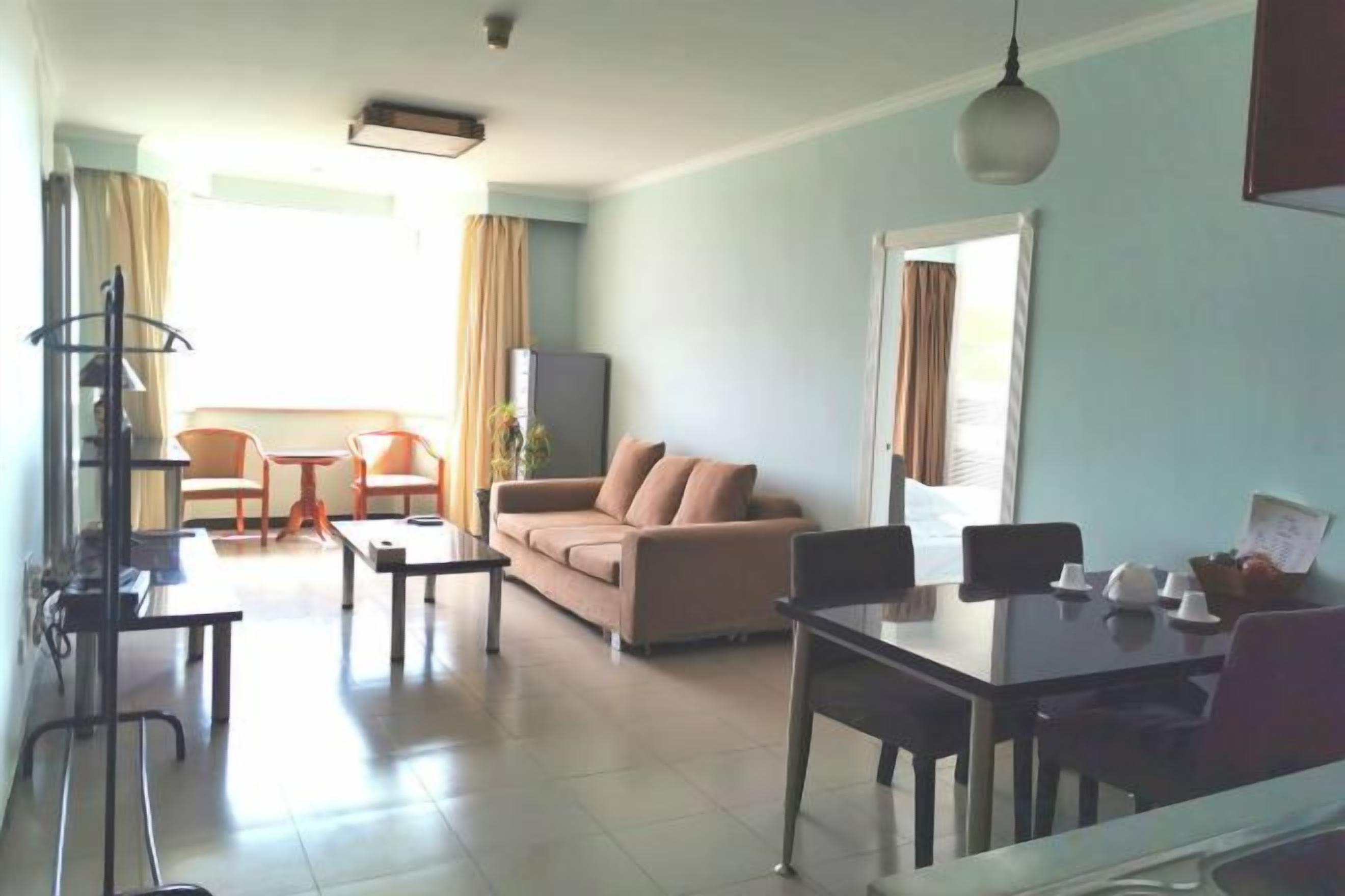A living room with a sofa, coffee table, and TV stand. There is a dining table with chairs.
