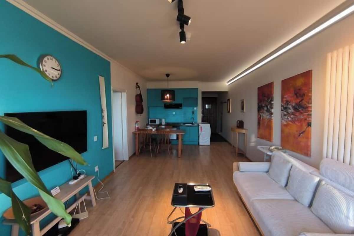 Een woonkamer met een televisie, bank en een eethoek met een tafel en stoelen.