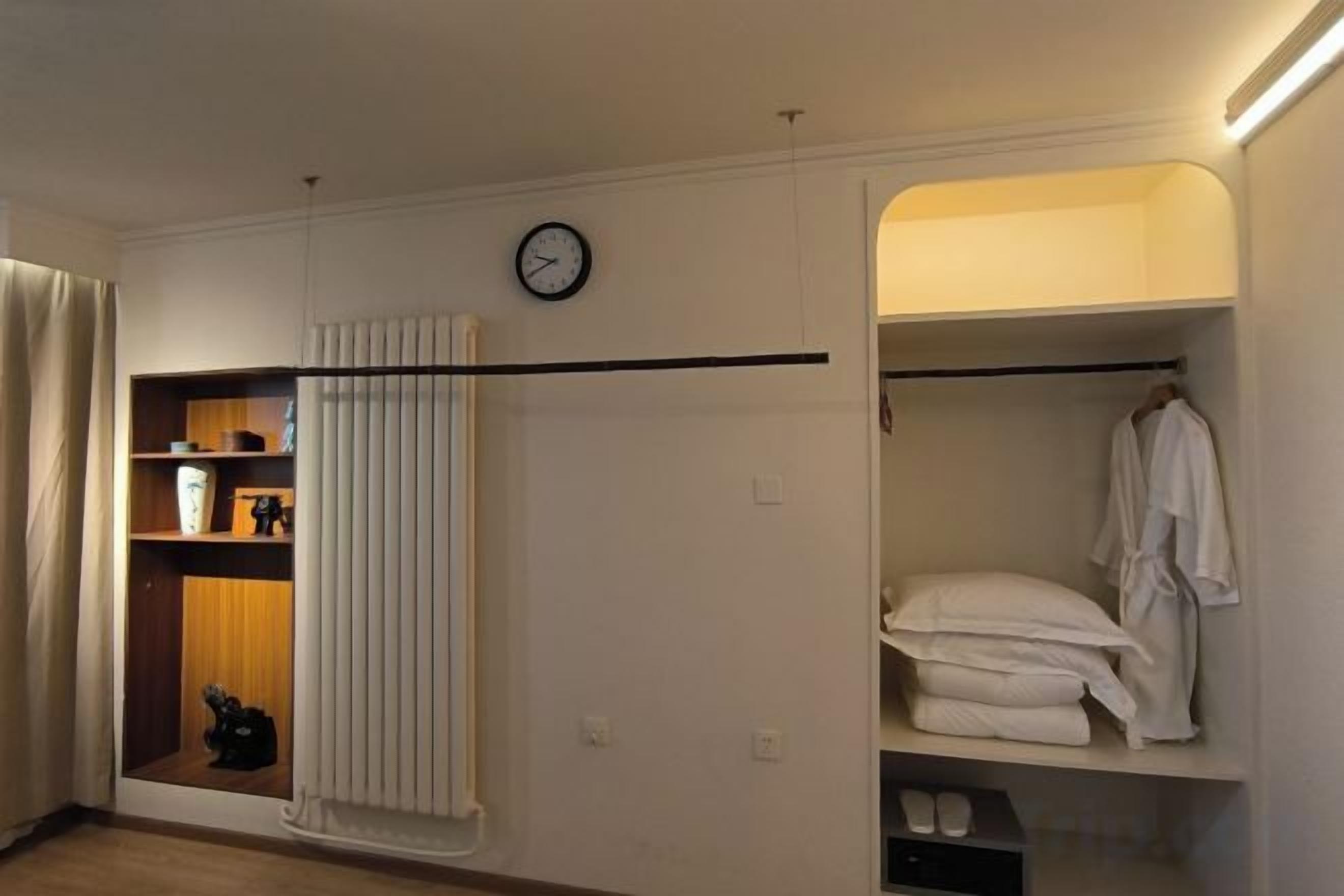 A hotel room with a built-in closet, a clock on the wall, and a radiator.